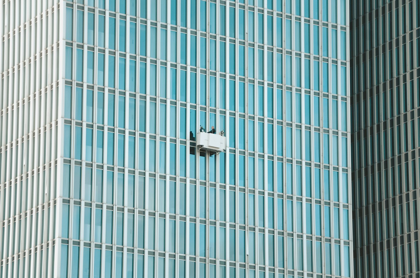 Workers on platform clean windows of modern office building.